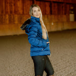 Woman wearing a blue puffer jacket with fur hood in an indoor setting