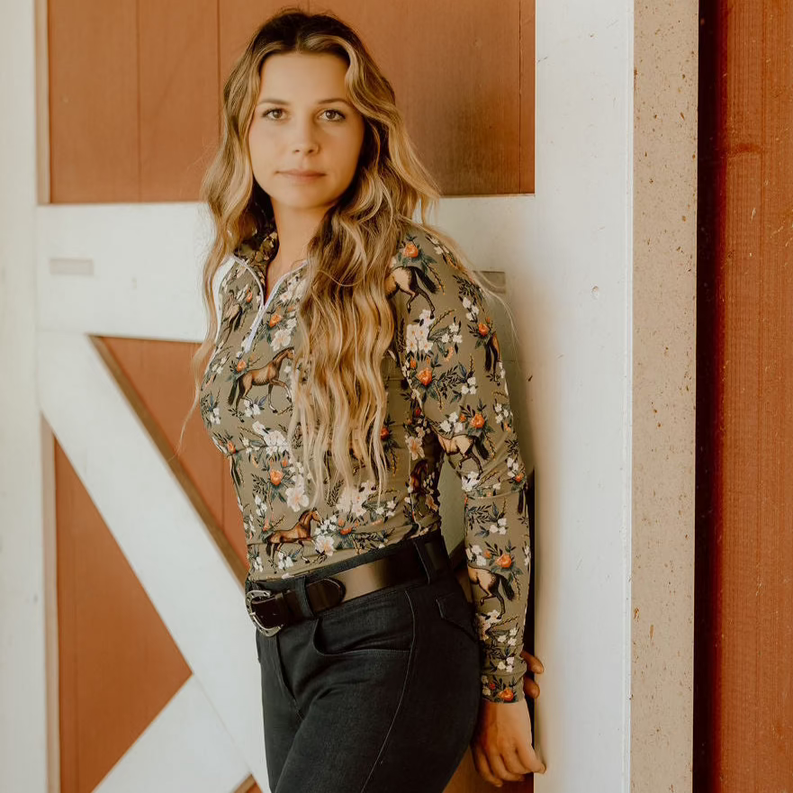 Woman wearing a floral blouse and dark pants standing against a barn door.