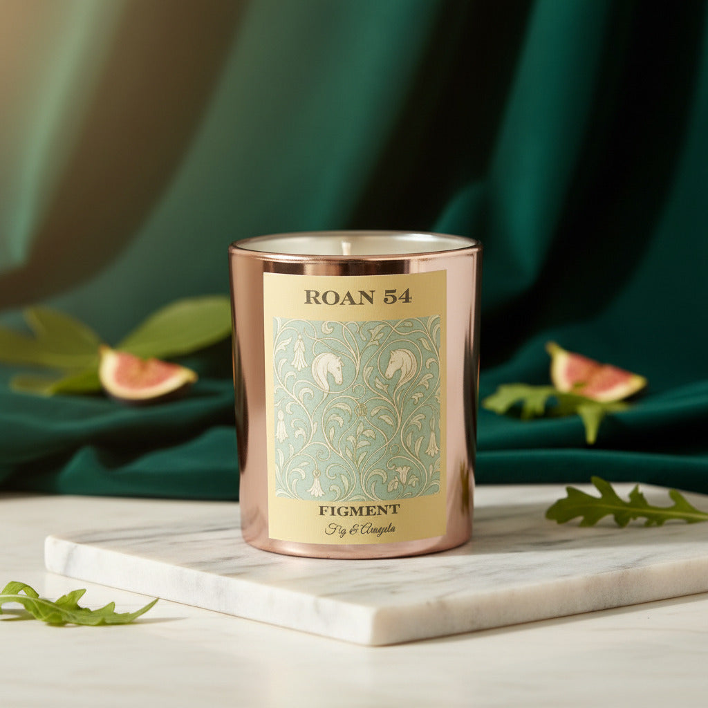 Rose Gold Fig & Arugula Candle with a decorative label on a marble surface with green leaves in the background