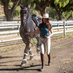 Woman leading a horse in an outdoor setting with trees and a fence in the background