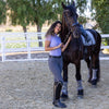 Woman in equestrian attire standing next to a horse in an outdoor setting