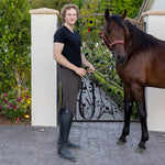 Man standing next to a horse on a paved area with a mountainous background